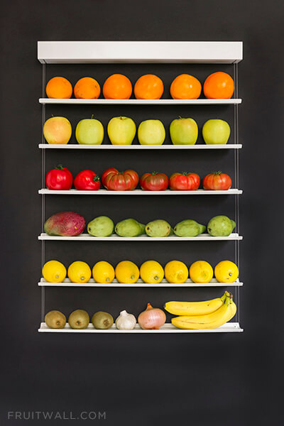 Fruteros de pared colgante con 6 estantes sobre fondo negro lleno de naranjas, manzanas, tomates, mango, peras, limones, kiwis, ajo, cebolla y platanos