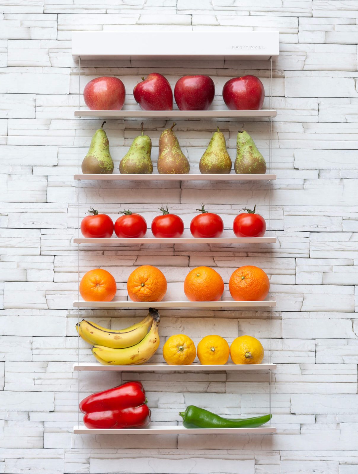 Fruitwall, los mejores fruteros modernos y de diseño para la cocina, colocado sobre pared de piedra blanca. Esta lleno de frutas y verduras. modelo 420